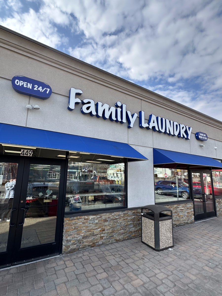 Exterior view of a family laundry store with large blue signs, blue awnings, glass doors, and windows, with parking lot and cars visible through the windows.