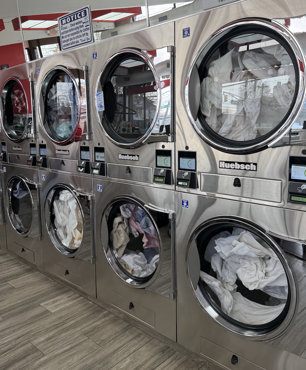 Dryer machines at a laundromat with clothes inside and a sign above.