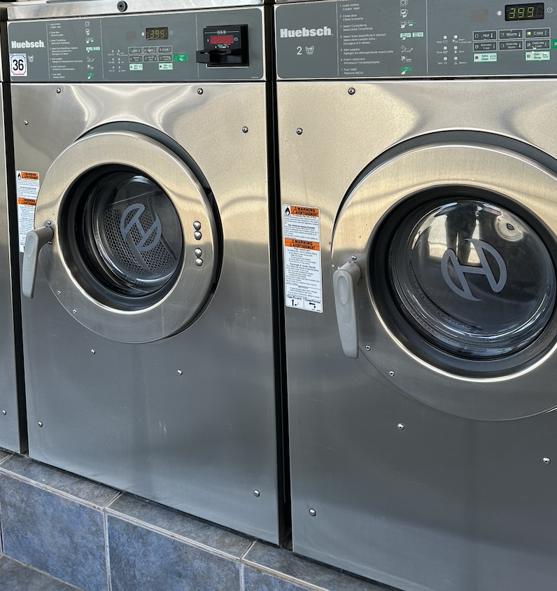 Front view of two stainless steel Huebsch commercial washing machines side by side in a laundry facility.