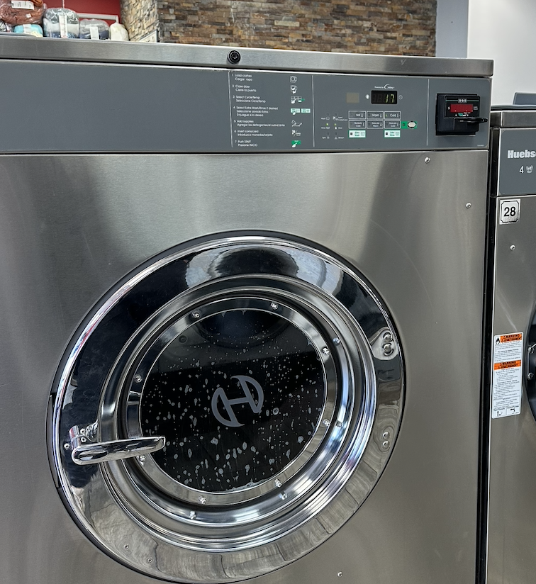 Front view of a stainless steel commercial washing machine with a round glass door and digital control panel.