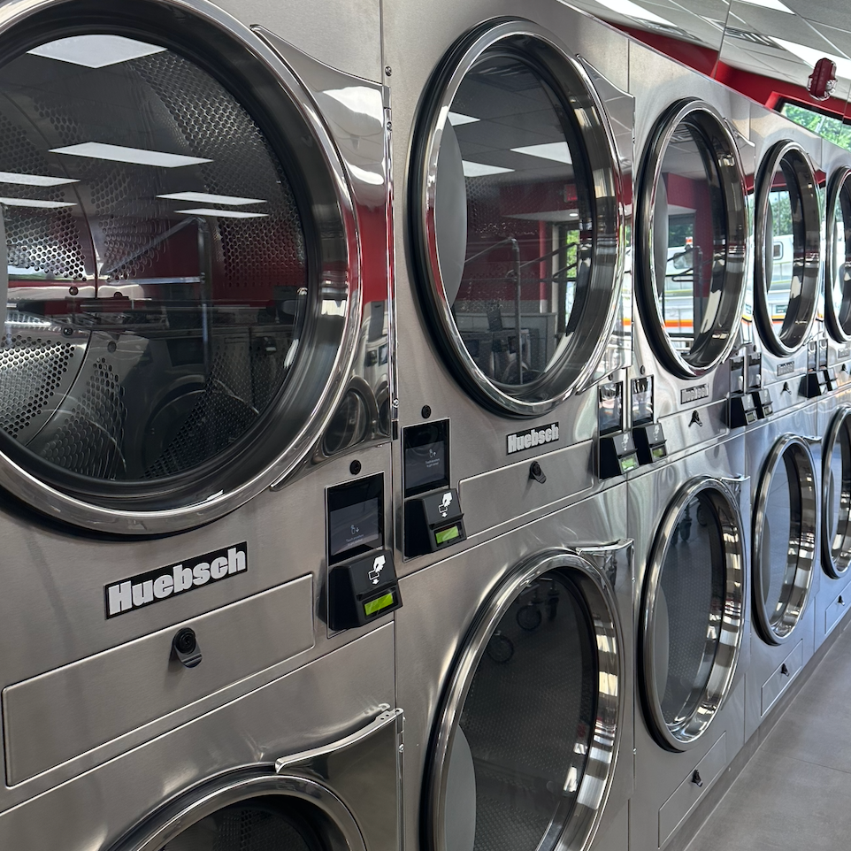 Row of stainless steel commercial washing machines in a laundromat.