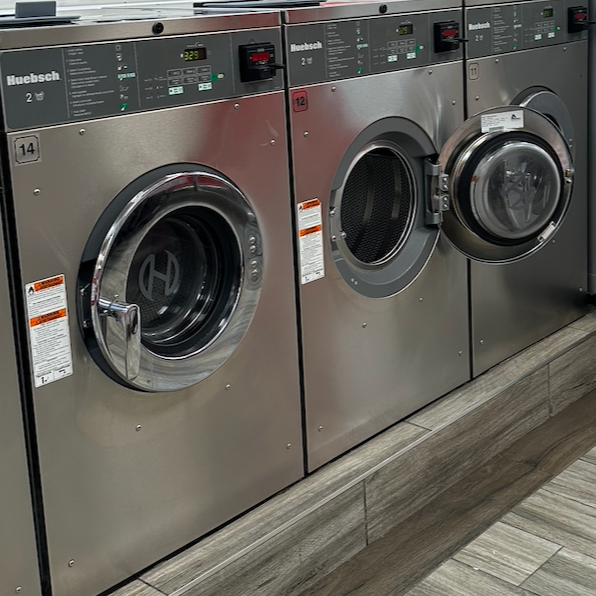 Three commercial washing machines in a laundry room with wooden flooring.