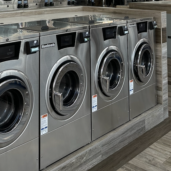 Stainless steel front-loading washing machines in a laundromat or laundry room.