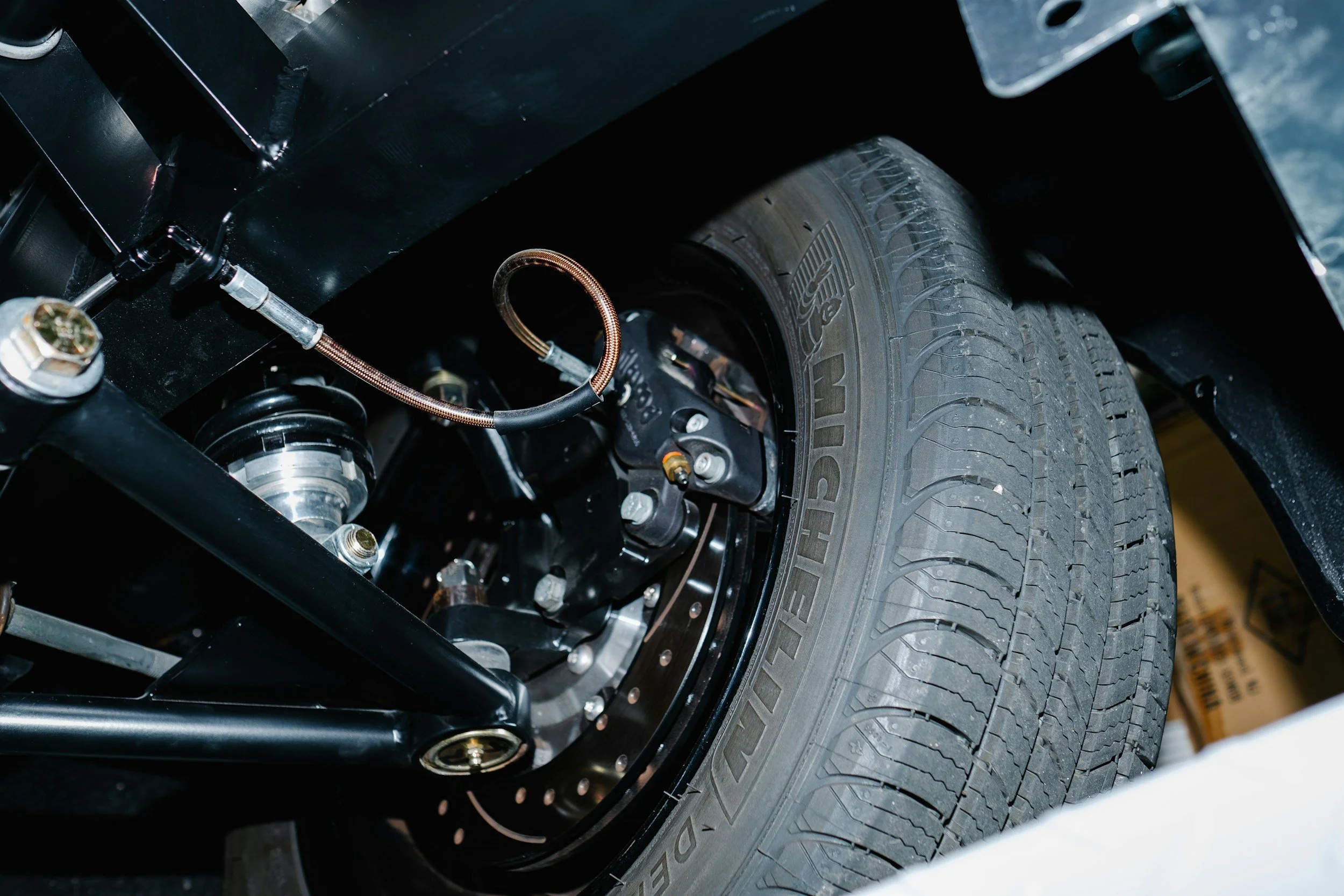 Close-up of a vehicle's suspension system and tire, showing metal components and hydraulic lines.