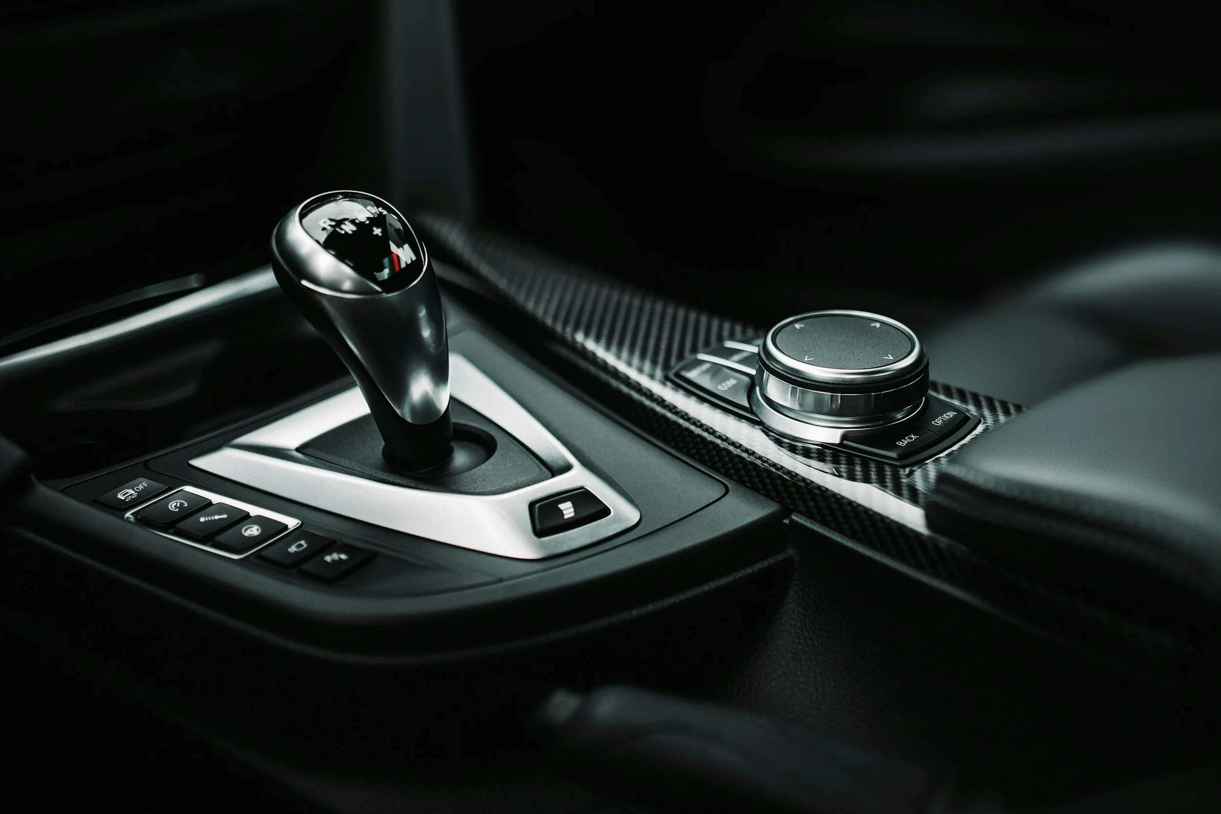 Close-up of a car's gear shift lever and control panel, with a textured gearshift knob and surrounding buttons.