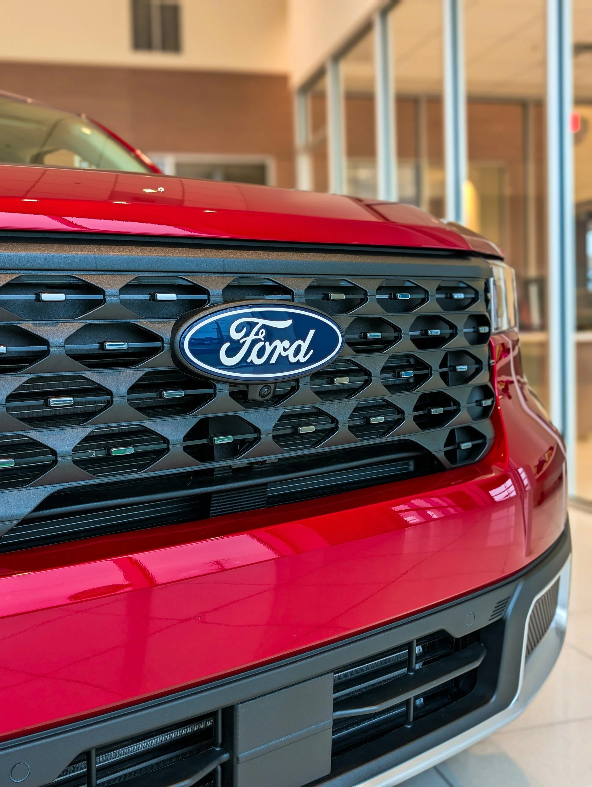 Close-up of the front grill of a red Ford vehicle, showing the Ford emblem and black grille design.