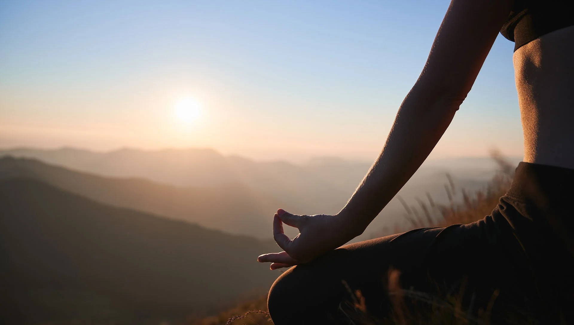 Persona sentada en la naturaleza haciendo meditación al amanecer con vista a las montañas y el sol naciente