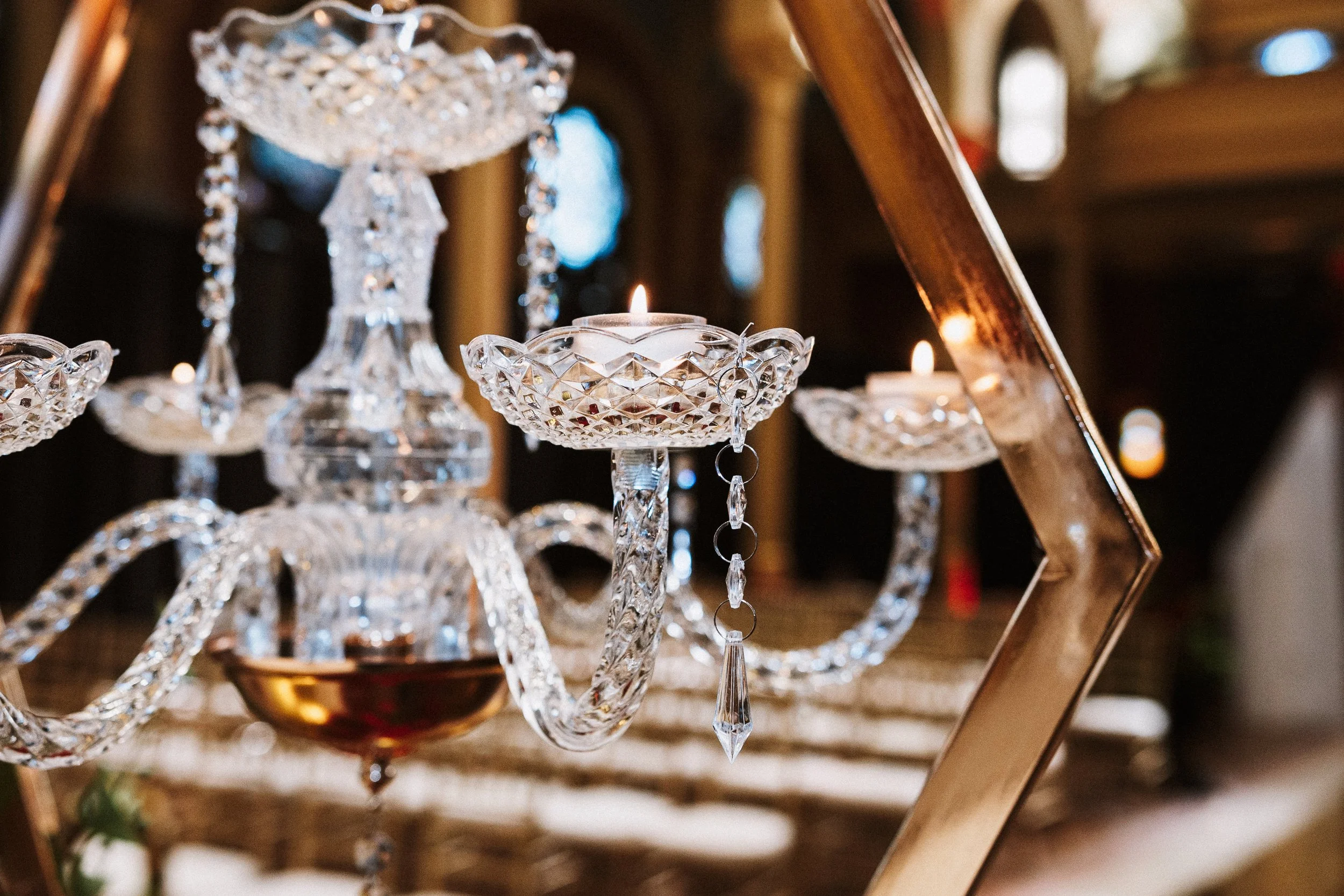 Close-up of a crystal chandelier with hanging pendants and a burning candle in a decorative holder, reflecting light in a dim interior setting.