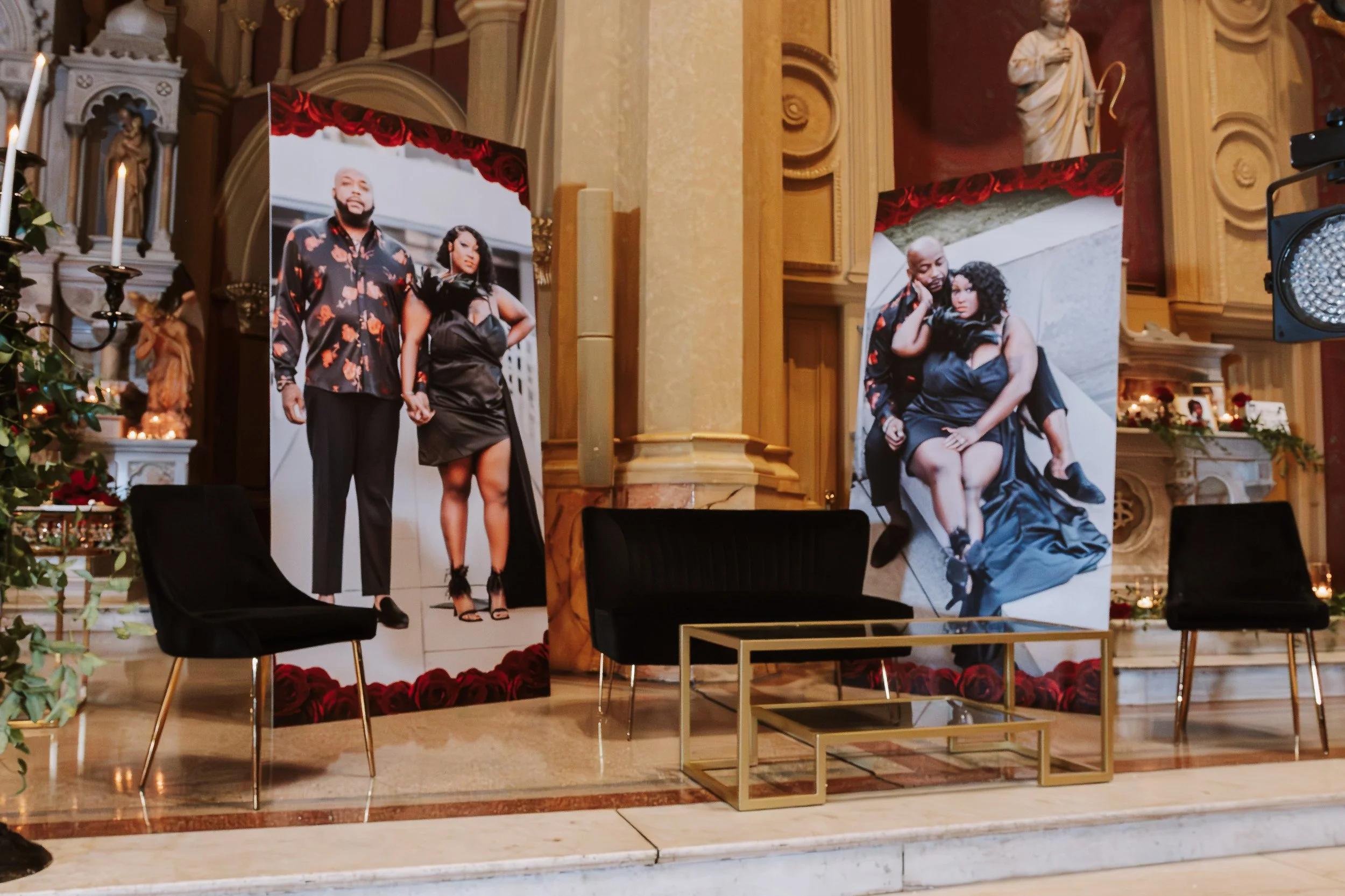 Interior of a church or cathedral with large posters of a man and woman, decorated with roses and statues.