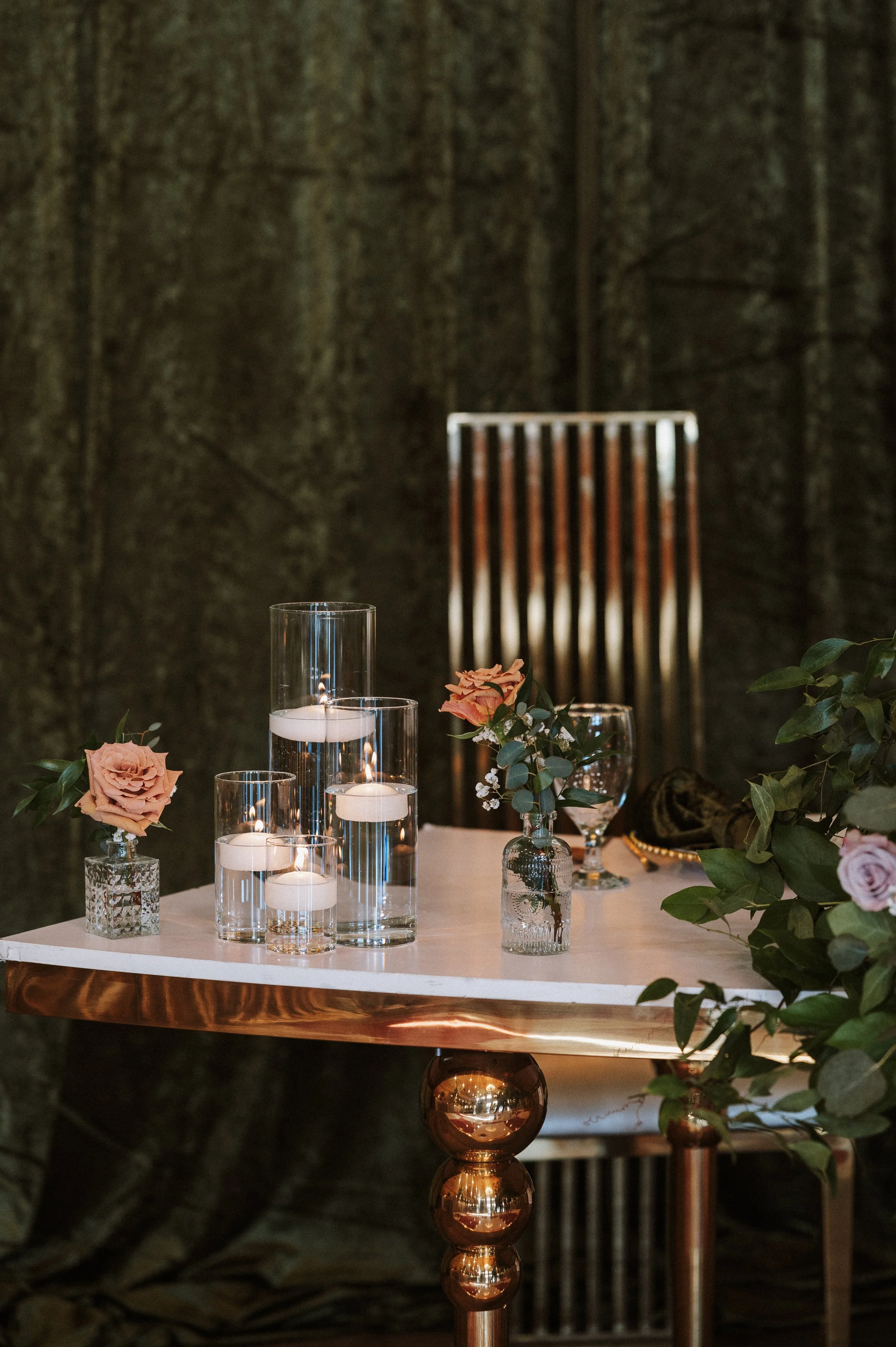 Decorative table with roses, candles, and glass vases, against dark textured background.