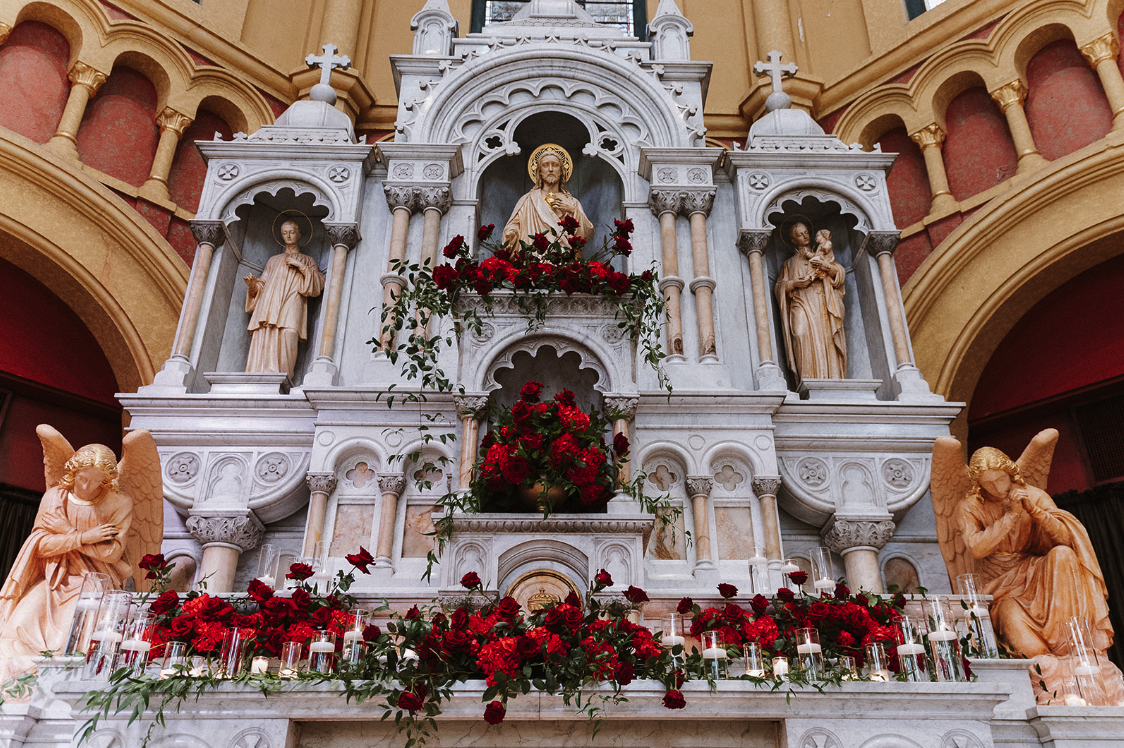 A religious altar decorated with red roses, featuring statues of Jesus Christ and angels in a church.