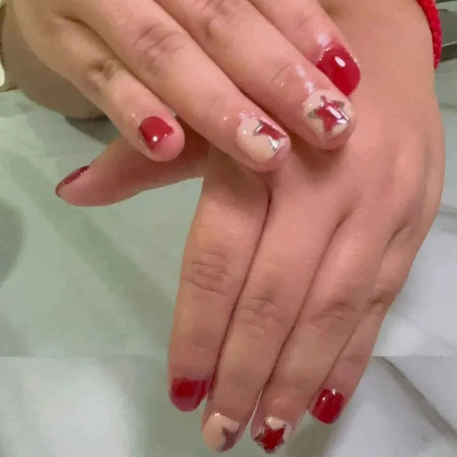 Mano con uñas pintadas de rojo y esmalte dañado con esmalte plateado