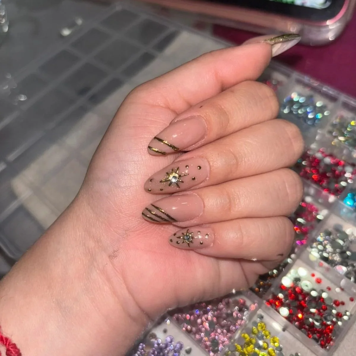 Uña decorada con diseño de estrellas y puntos pequeños con detalles dorados y brillantes, sobre un fondo de uñas desnudas.