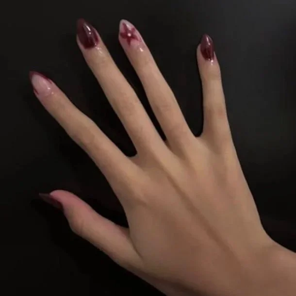 Mano con uñas pintadas y decoradas con esmalte en tonos oscuros y detalles en color rosa y blanco.