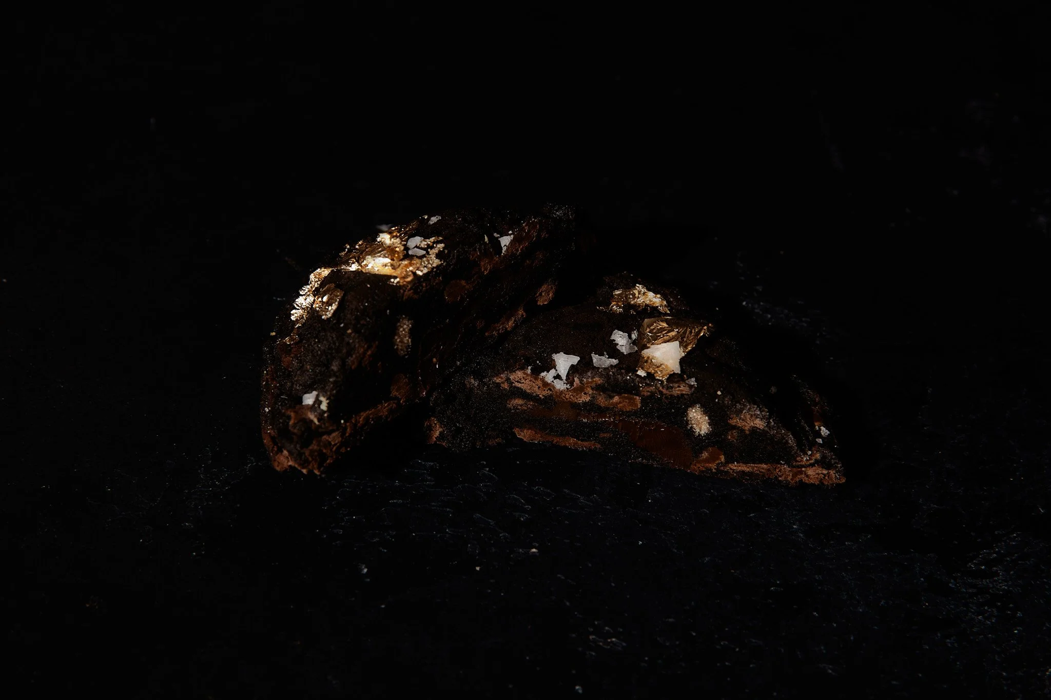 Dark chocolate truffles sprinkled with sea salt on a black surface.