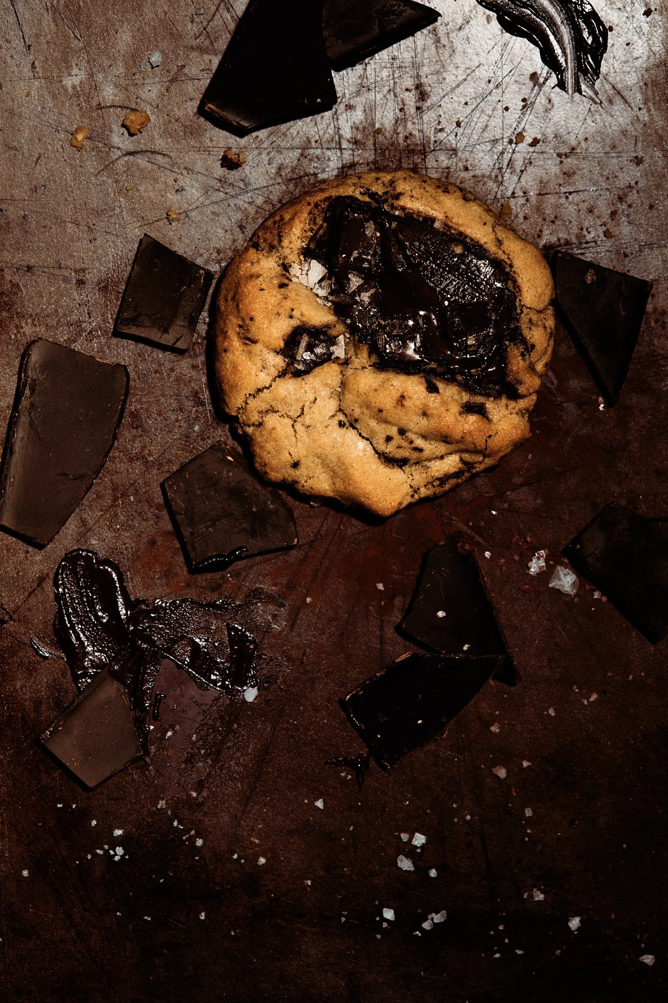 A partially eaten chocolate chip cookie with broken pieces of chocolate on a dark surface.