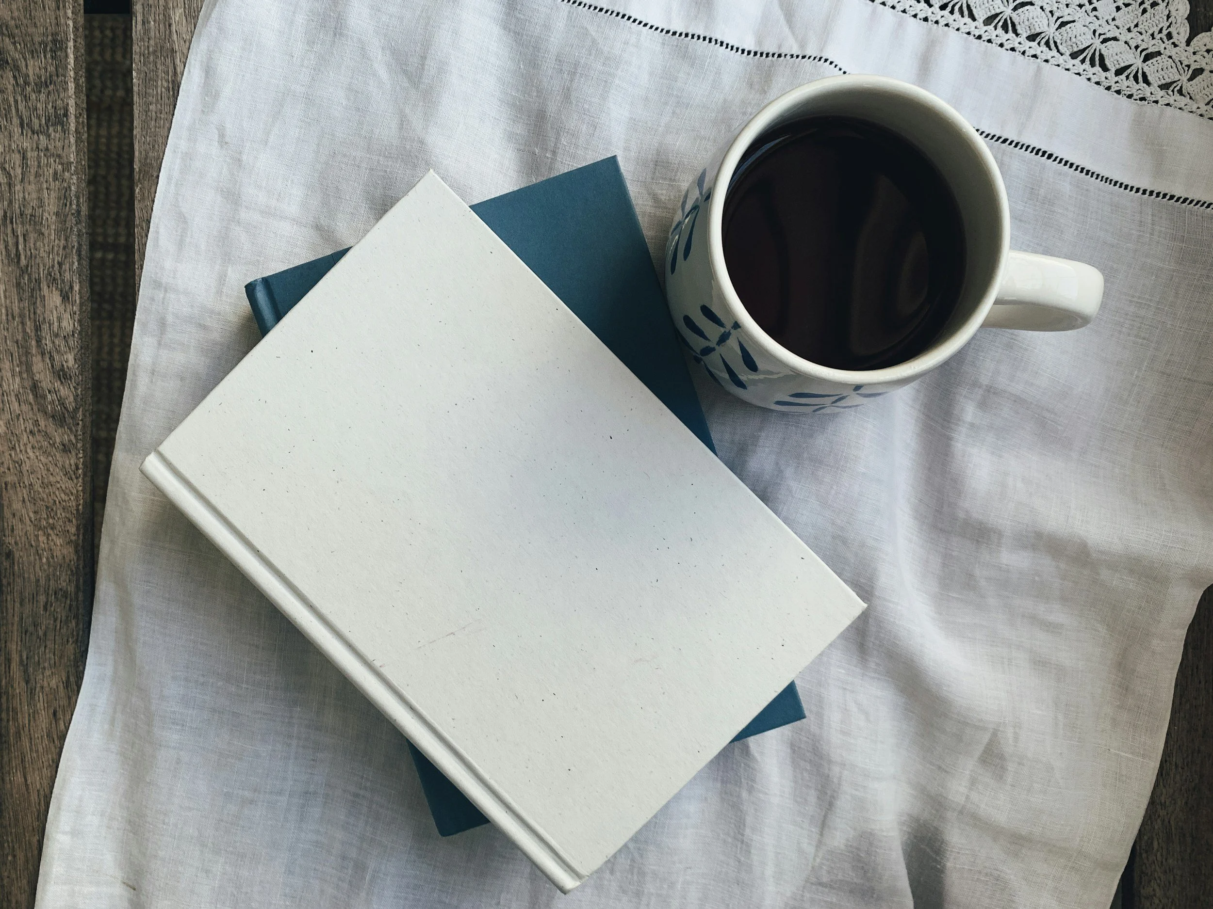 Stacked notebooks and a cup of coffee on a linen cloth, representing organized bookkeeping and a calm, detail-oriented approach to small business finances.