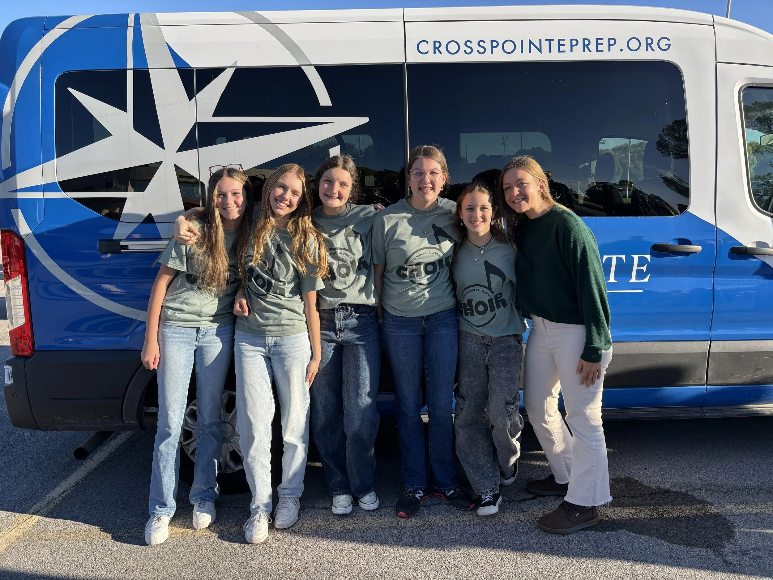 Group of six young women standing in front of a large van with the website 'crosspointerpr.org' on it, posing outdoors on a sunny day.