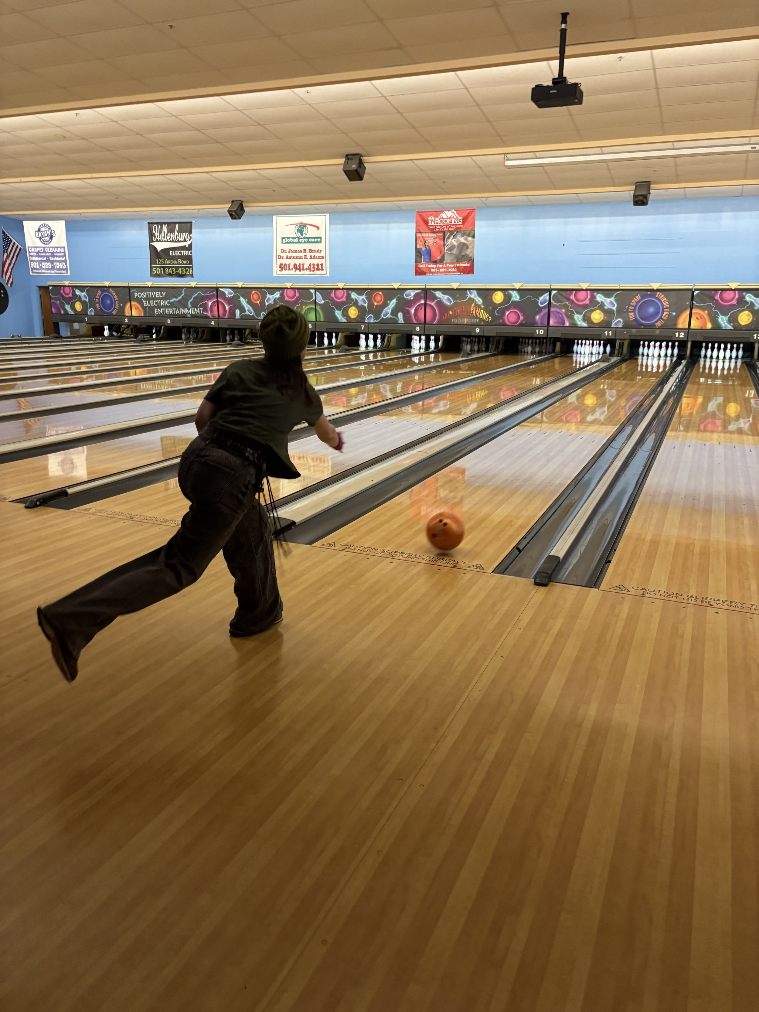 Person bowling a ball on a bowling alley, with pins set up at the end of the lane and colorful decorative graphics on the bowling pin area.
