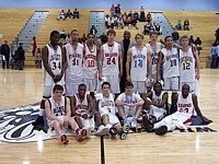 Basketball team photo on the court, players in white jerseys, some sitting and some standing.