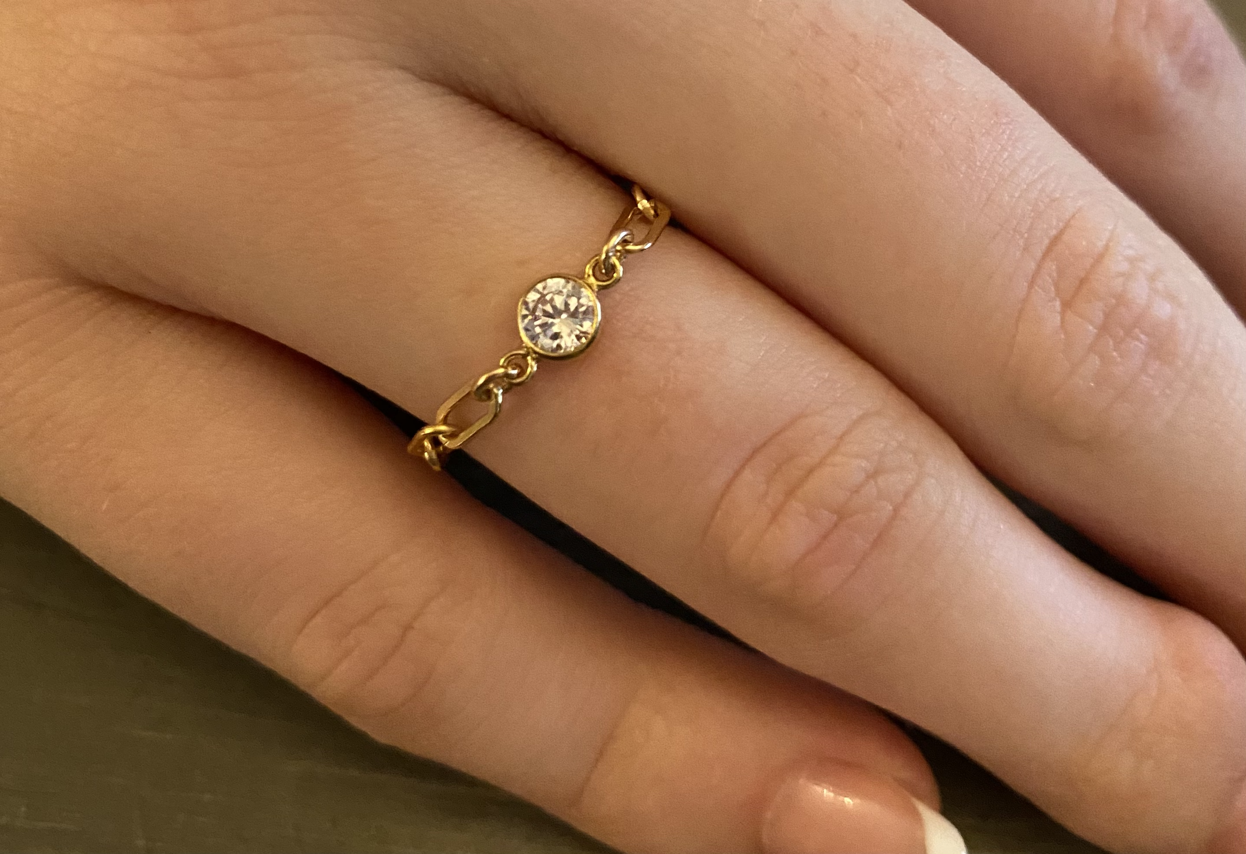 Close-up of a person’s finger wearing a gold ring with a clear gemstone, with a wedding band underneath.