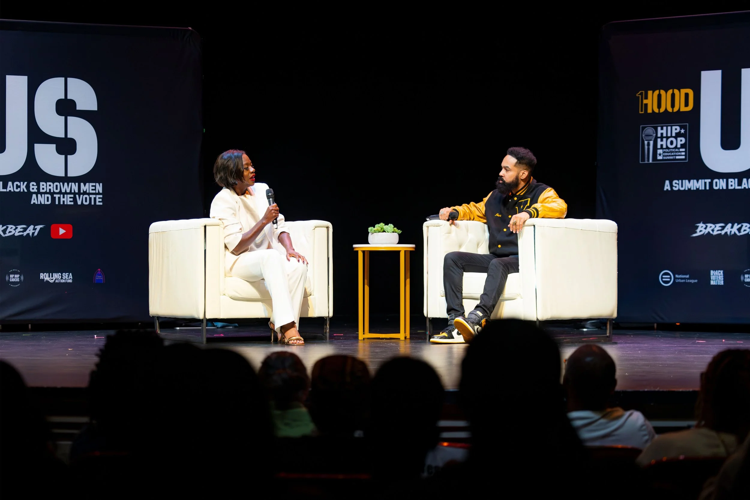 A woman and a man are having a conversation on stage at a 1Hood event