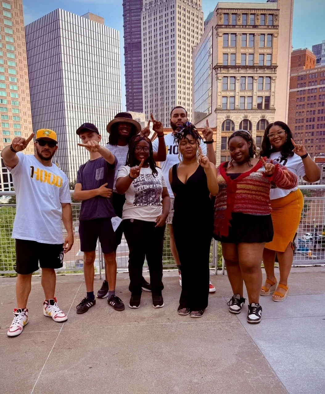 Group of diverse people standing outdoors in an urban setting with tall buildings, some making gestures with their hands, smiling and posing for the photo.