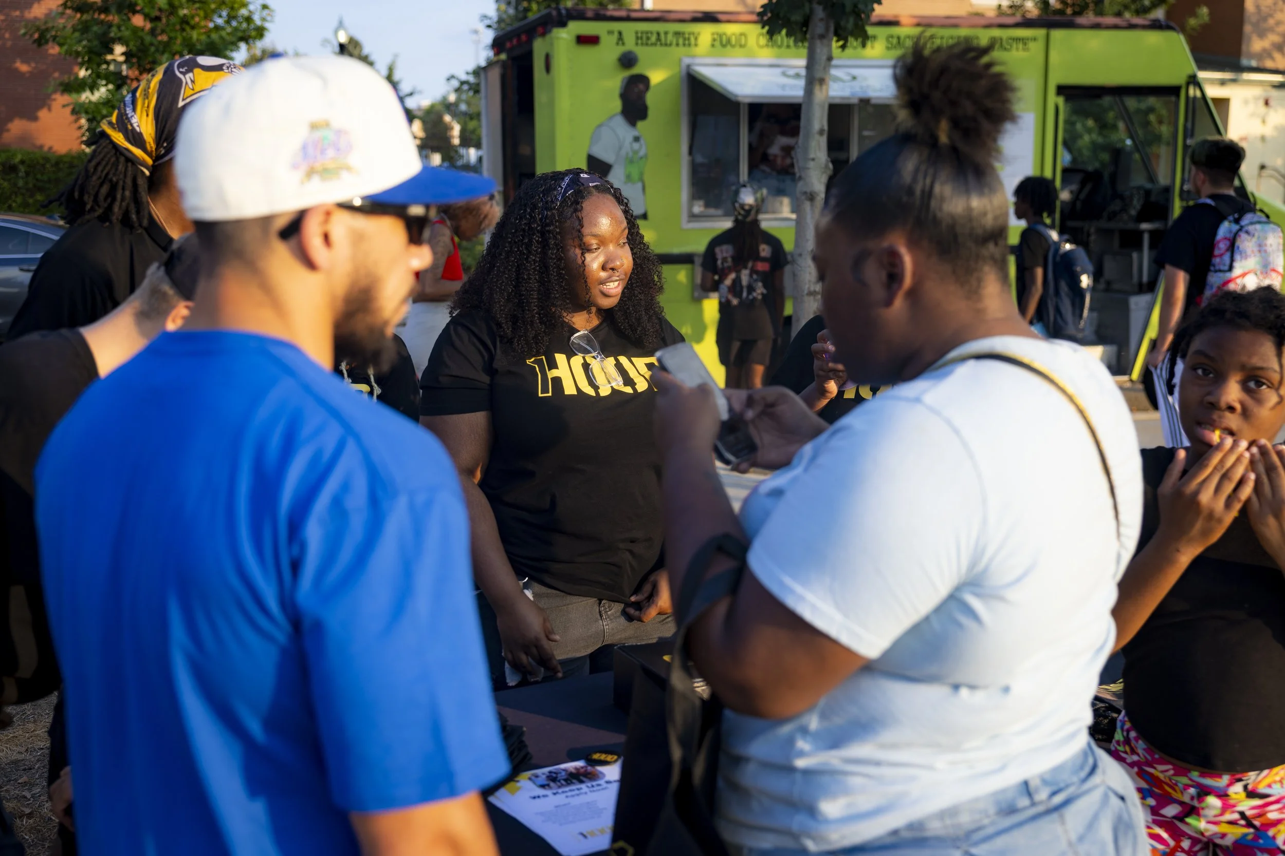 A group of people gathered outdoors at a food truck event, talking and engaging in the community event.