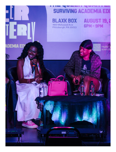 Two women sitting on a stage with a table in front of them, microphones, and drinks, during a panel discussion at an event.