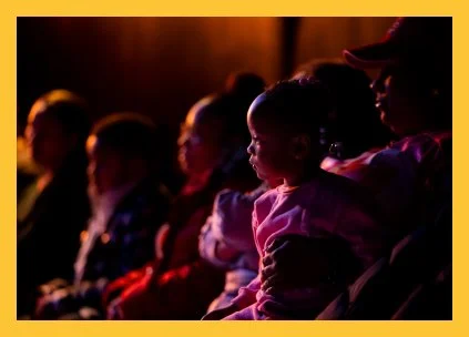 People watching a performance in a dimly lit theater.