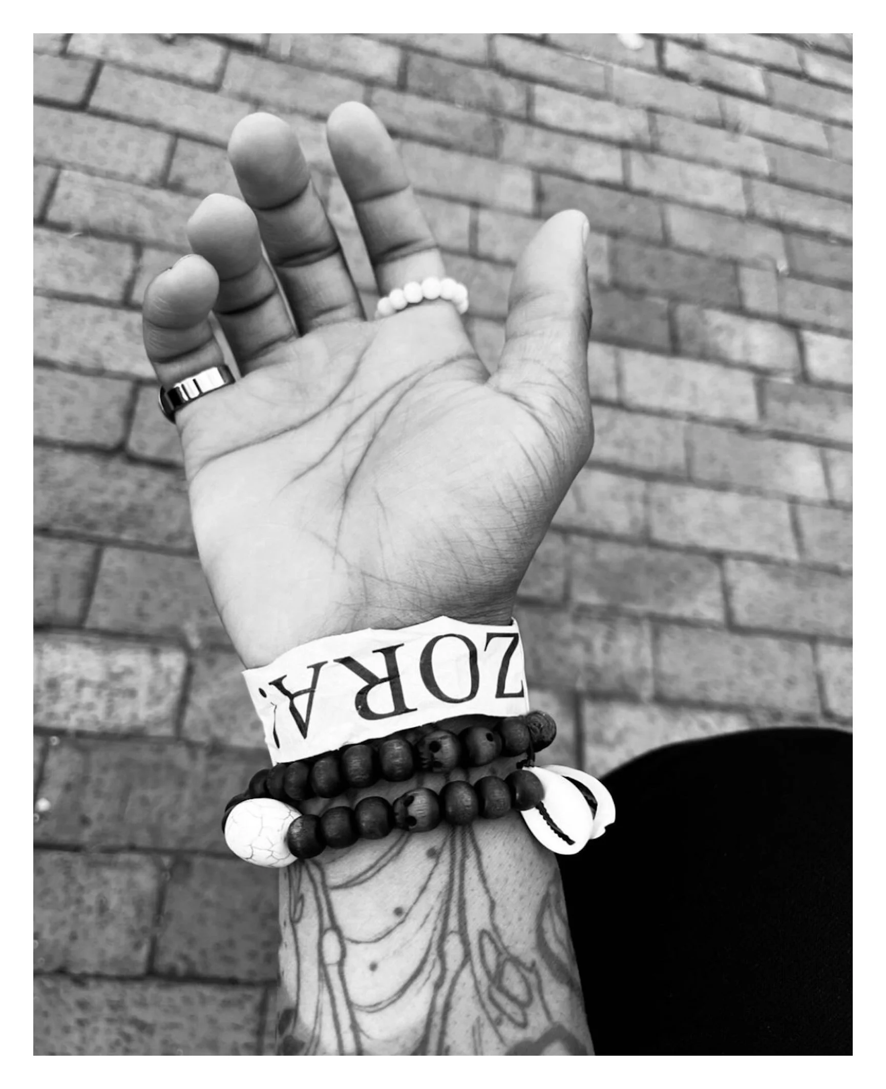 Close-up of a hand wearing a ring and bracelets in front of a brick wall background.