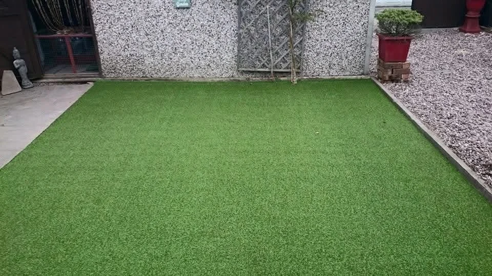 Artificial grass lawn in a backyard with concrete and gravel areas, potted plants, and a lattice fence.