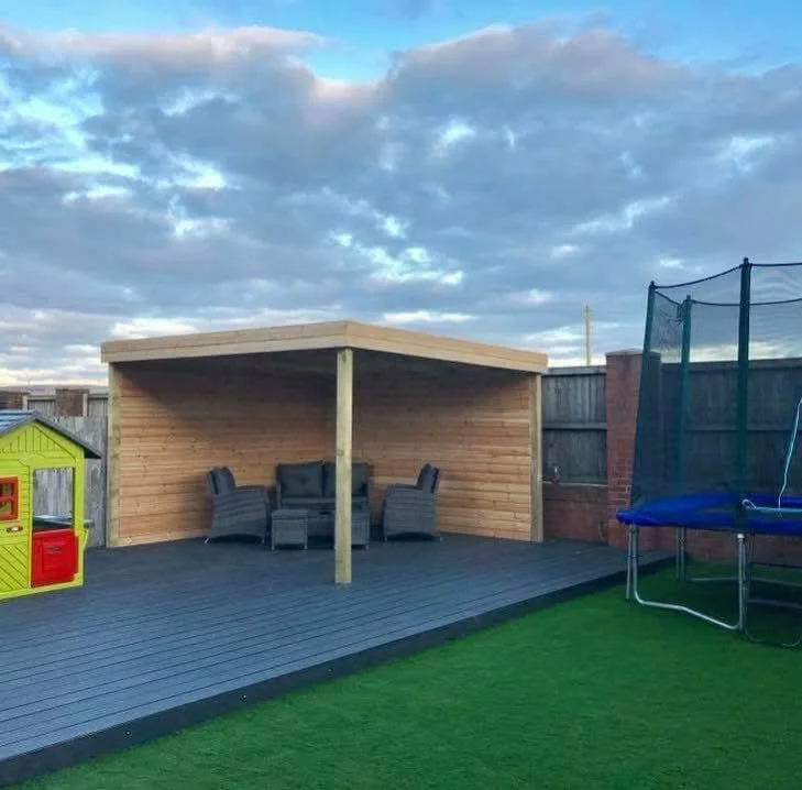 Backyard with wooden gazebo, outdoor seating, children's playhouse, trampoline, and artificial grass under a partly cloudy sky.