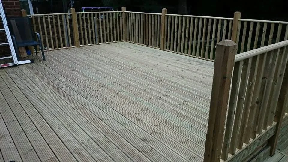 Empty wooden deck with railing and a plastic chair at the corner, surrounded by trees.
