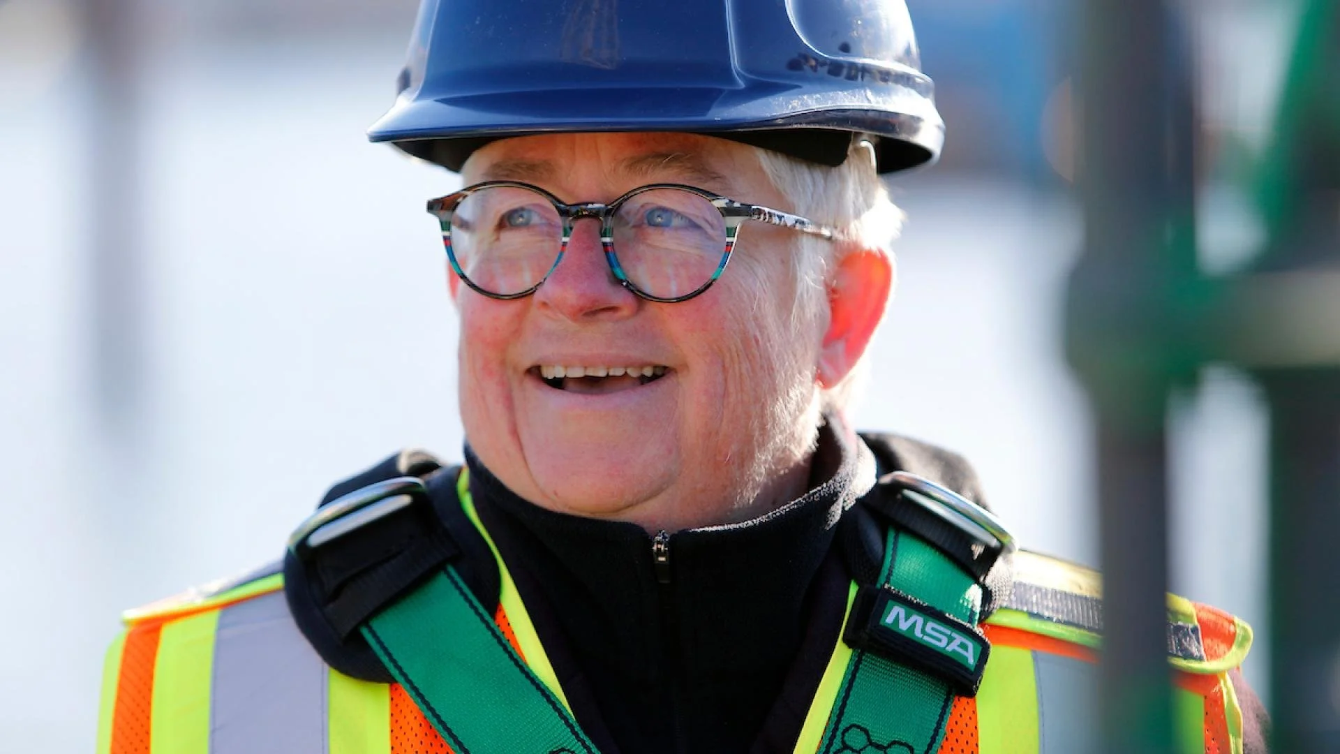 Marianne wears a hard hat and safety equipment, smiling while looking to the right.