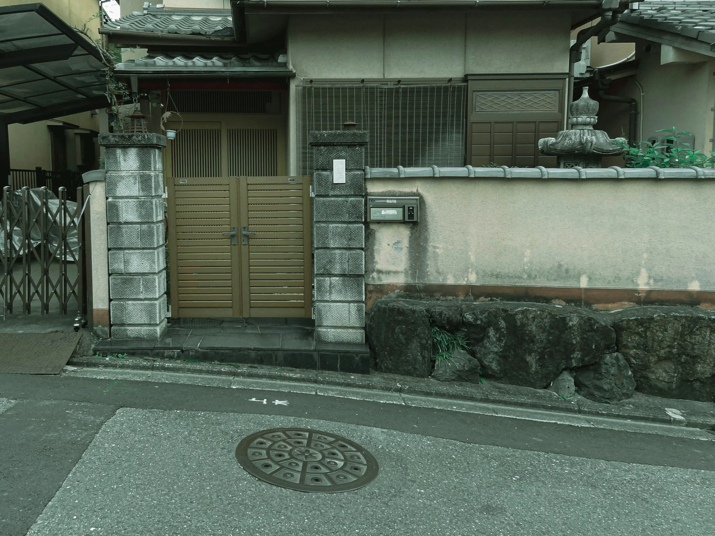 Street view of a traditional Japanese house gate with high stone walls, a sliding door, and a mailbox mounted on the wall.