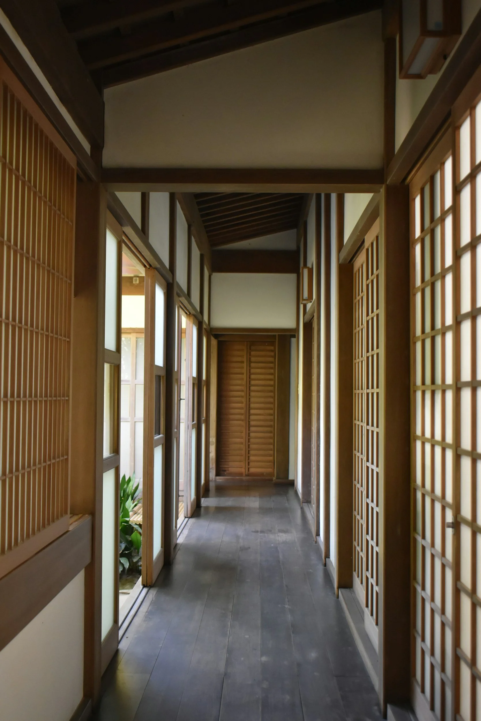 A narrow, traditional Japanese-style interior hallway with wooden sliding lattice doors and windows, leading to a closed wooden door at the end.