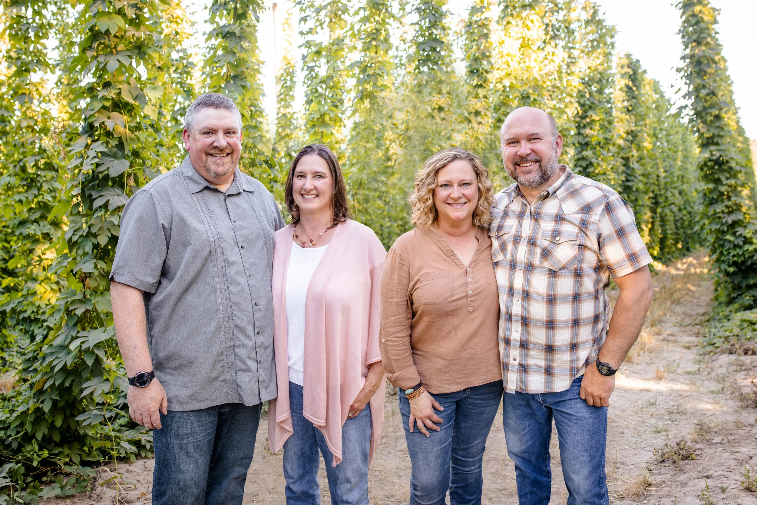 Four people standing together outdoors in a green plant field, smiling at the camera.