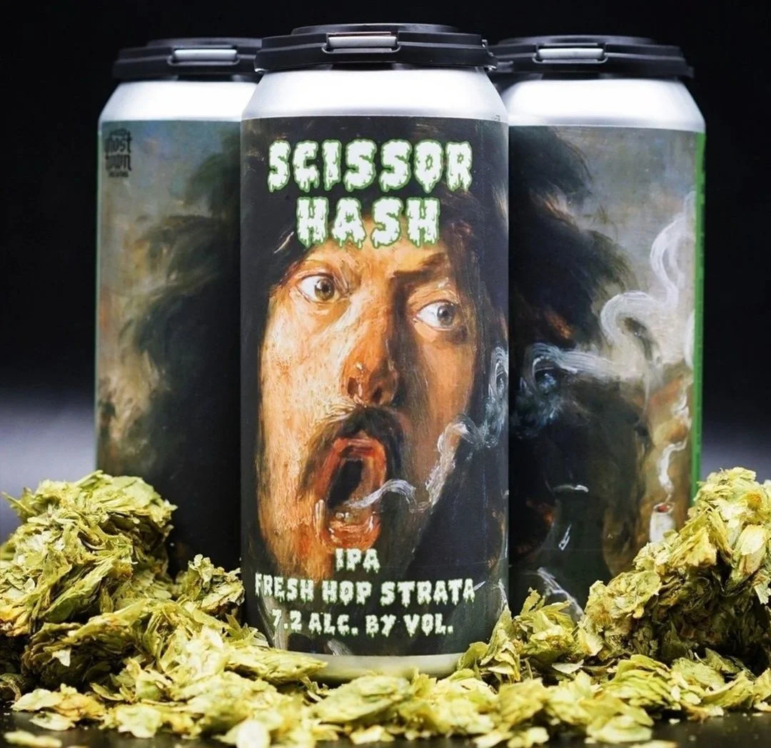 Cans of Scissor Hash IPA with a painted face on the label, surrounded by fresh hops.