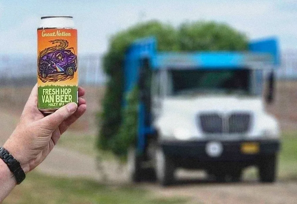 Person holding a Great Notion Fresh Hop Van Beer can in front of a truck loaded with fresh hops, outdoor setting.