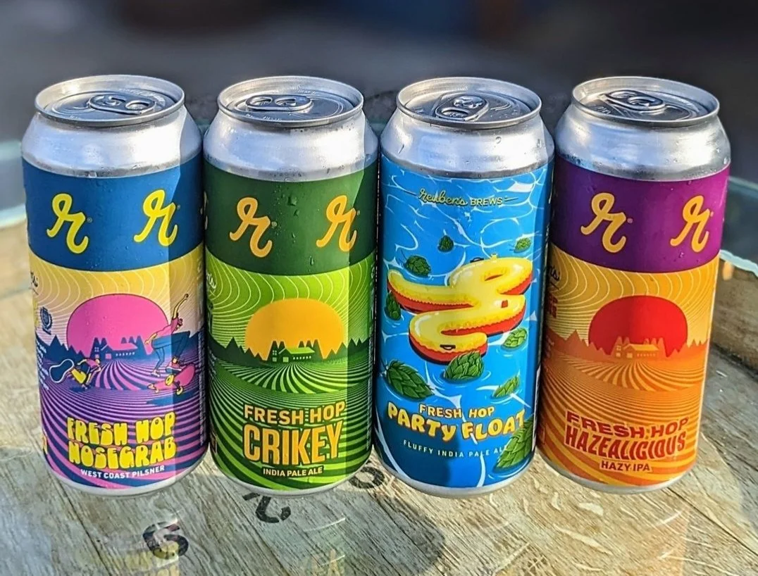 Four colorful beer cans featuring Reuben's Brews branding with different labels: Fresh Hop Nosegrab, Fresh Hop Crikey, Fresh Hop Party Float, and Fresh Hop Hazalicious.