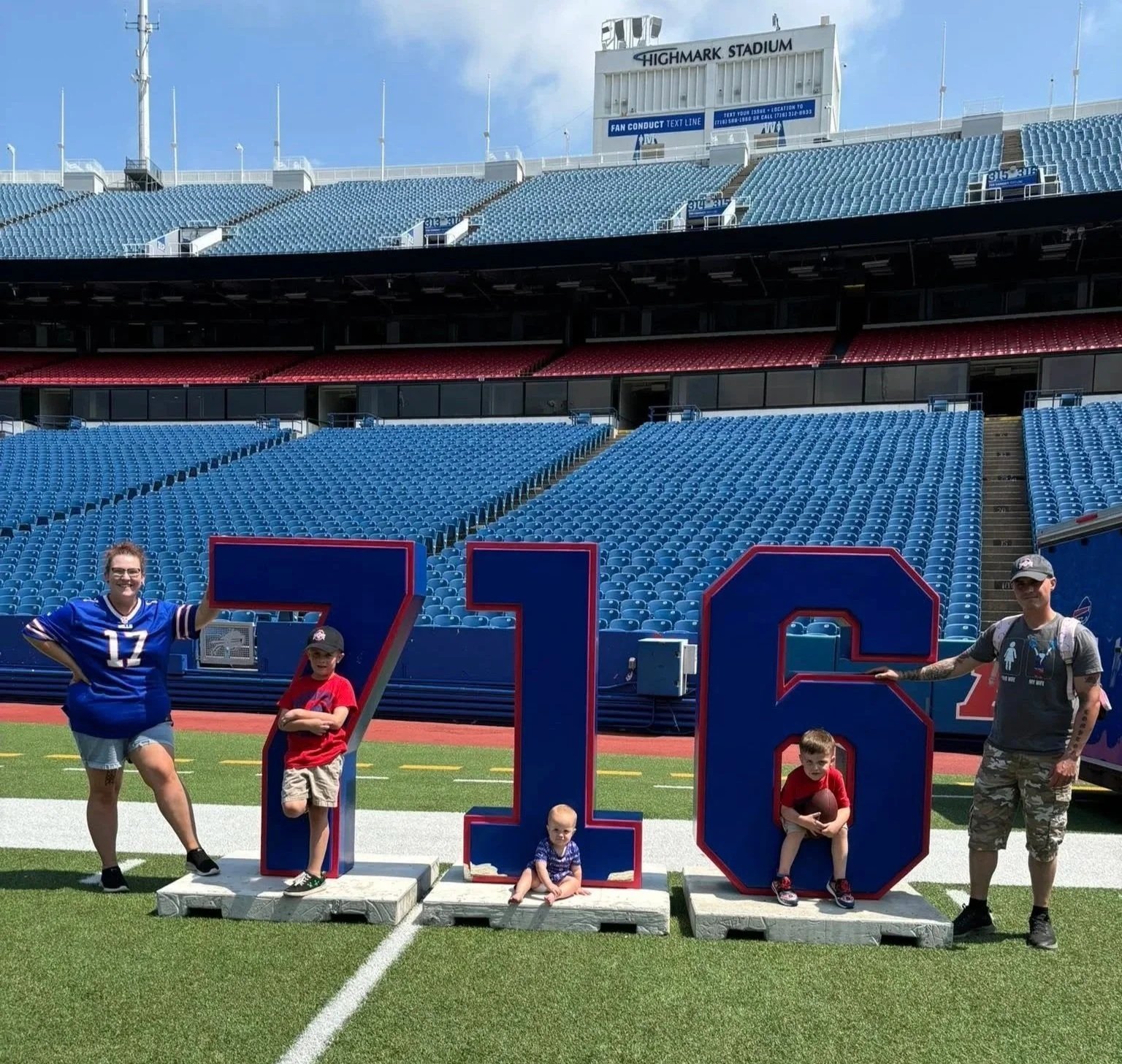Family on a football field with large red, white, and blue numbers 7, 1, 6, holding footballs at Highmark Stadium, with empty blue stadium seats in the background.
