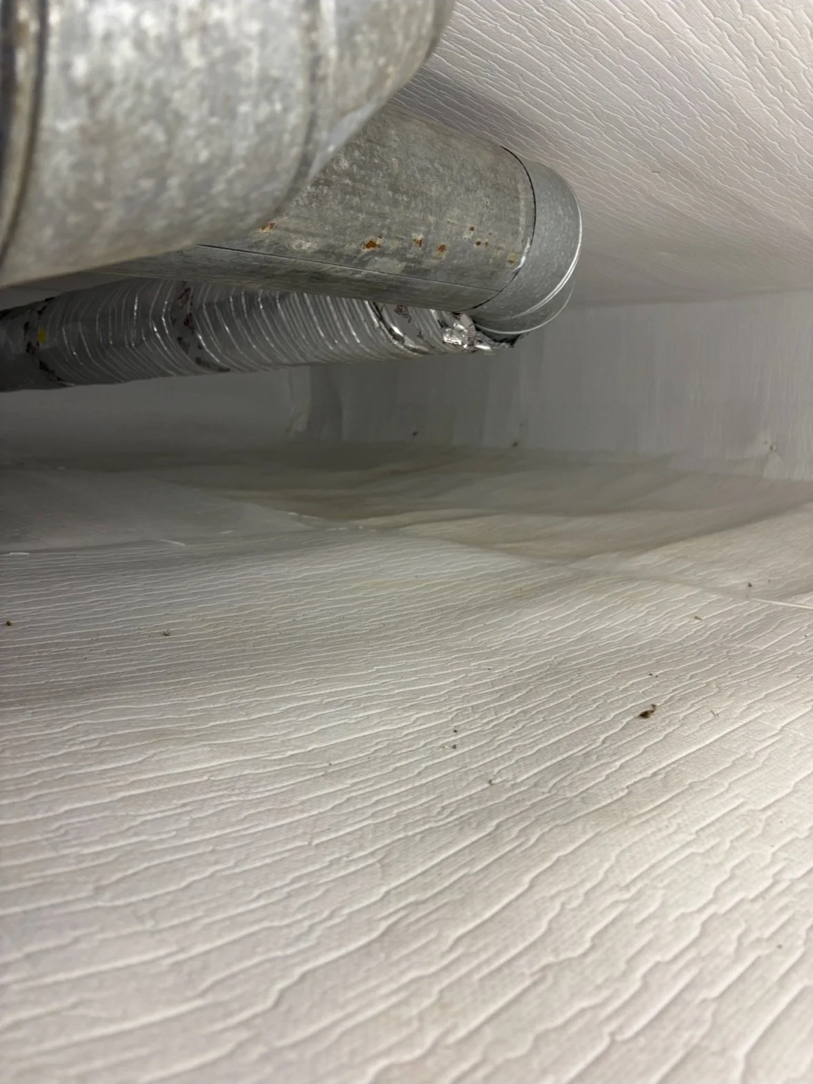 Close-up view of a section of ductwork beneath a ceiling or floor, with some rust spots visible on the metal surface.