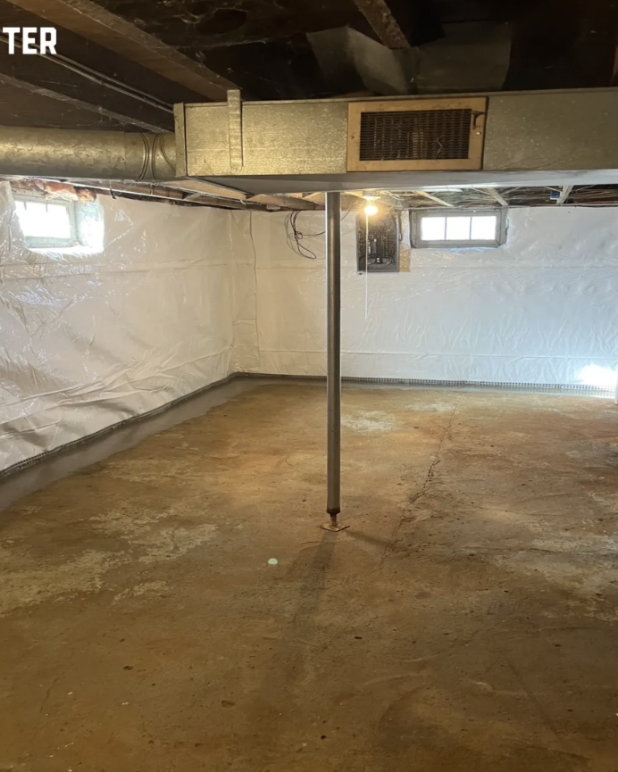 Basement with concrete floor, white insulating walls, small windows, and a support pole in the center.