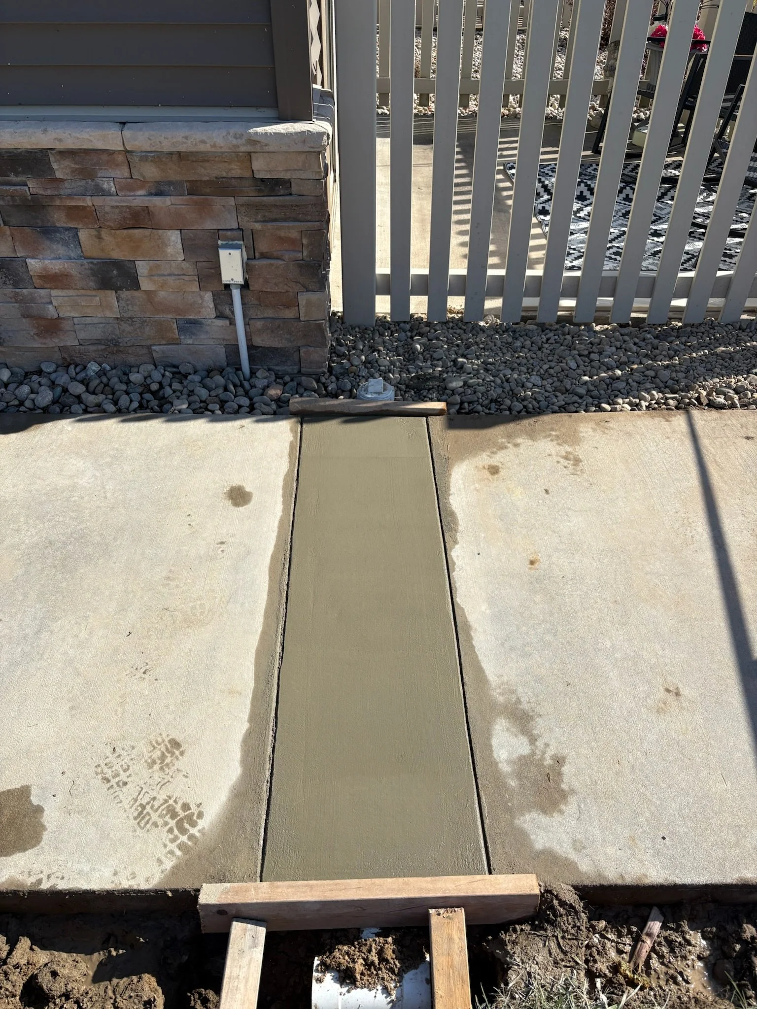 Freshly poured concrete being smoothed in a sidewalk section, with wooden forms and gravel surrounding the area.