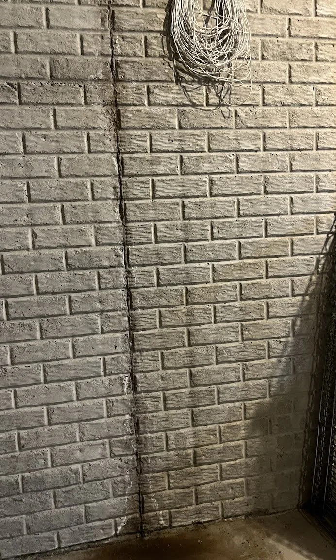 A brick wall with a vertical crack and some electrical wires hanging from the top