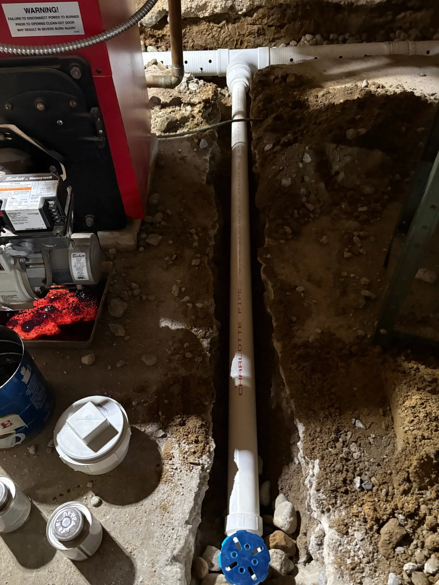 A plumbing installation in a trench with PVC pipes, a blue valve, and construction tools and materials nearby.