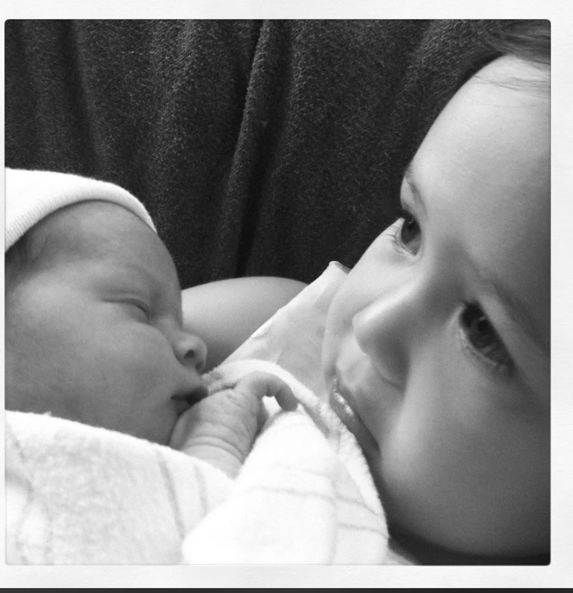 A young girl gently touching a baby’s nose as they lie close together.