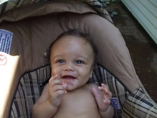 A baby sitting in a car seat outdoors, with a puzzled or confused expression.