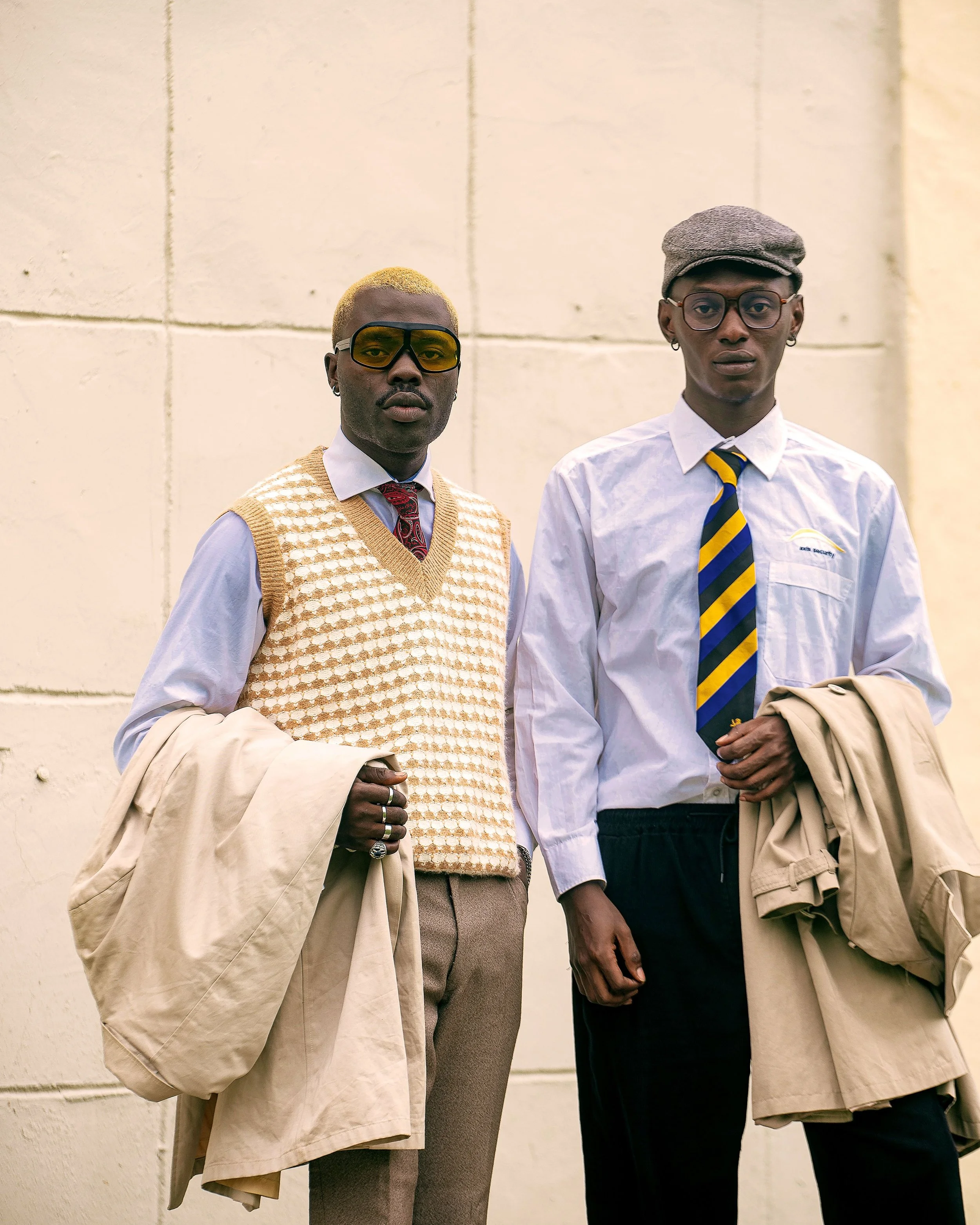 Two young men dressed in vintage-inspired fashion standing against a plain wall.